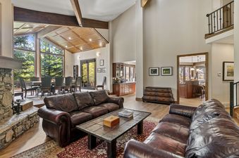 Living room with a fireplace and large windows overlooking a wooded area.