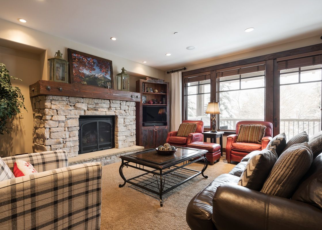 A cozy living room with a stone fireplace, plush seating, and large windows offering a winter view at Silver Star 902.