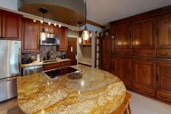 A kitchen with dark wooden cabinetry, stainless steel appliances, and a large granite island countertop.