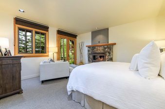 A bedroom with a fireplace, a couch, and a window with a view of the trees. The room is decorated in a modern style with white walls and wooden accents.