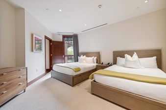 Two queen beds with white linens and yellow blankets are in a bedroom with wood furniture, a window, and a door leading to a patio.