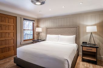 A king-size bedroom at Cedar Crest Sparrow Cottage 1 featuring a bed with white linens, two nightstands with lamps, a window, and a wooden floor.