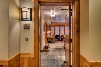 A wooden door with a metal handle opens to a hallway, leading to a living room with a couch and a coffee table.