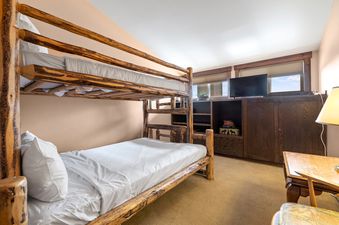 Cozy bedroom in Snowridge 6 with a rustic log bunk bed, wooden built-ins, and a television.