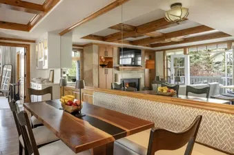 A large open concept room at Chateau Beaver Creek Residence 202 featuring a wooden dining table with a built-in banquette, leading into a living area with a fireplace and large windows showcasing an outdoor view.