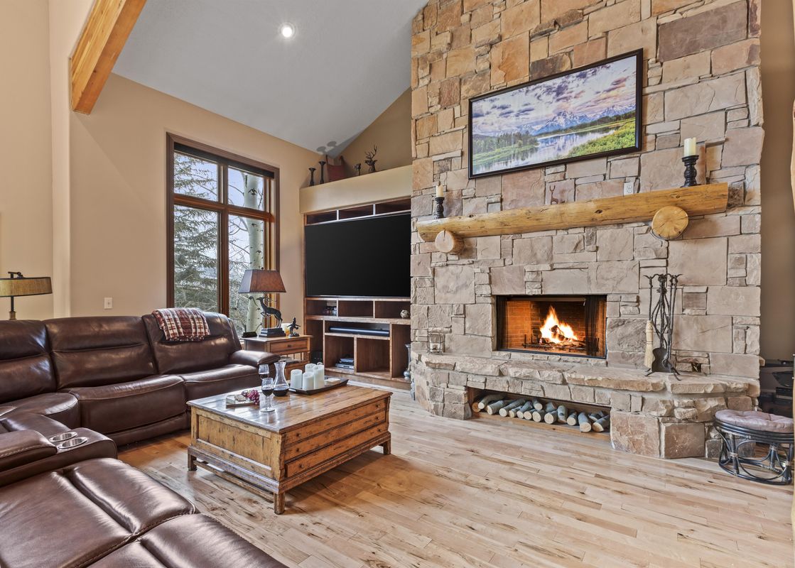 The living area in Cove Retreat is warmly lit and features a stone fireplace, leather seating, and wooden coffee table.