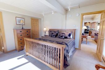 A cozy bedroom at Top of the Village Summit 103 featuring a wooden bed, patterned bedding, and rustic furnishings, with an open doorway leading to a kitchen.
