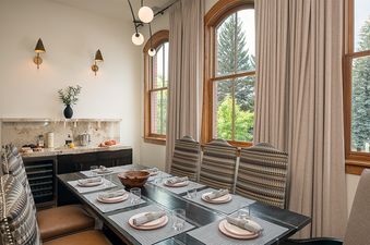 Elegantly set dining table with patterned chairs next to large arched windows with mountain views in the 5th Street Penthouse.