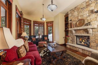 A cozy living room at the Chateau at Timber Trail features a large stone fireplace, a rich red sofa, and elegant wooden furniture, creating a warm and inviting atmosphere.