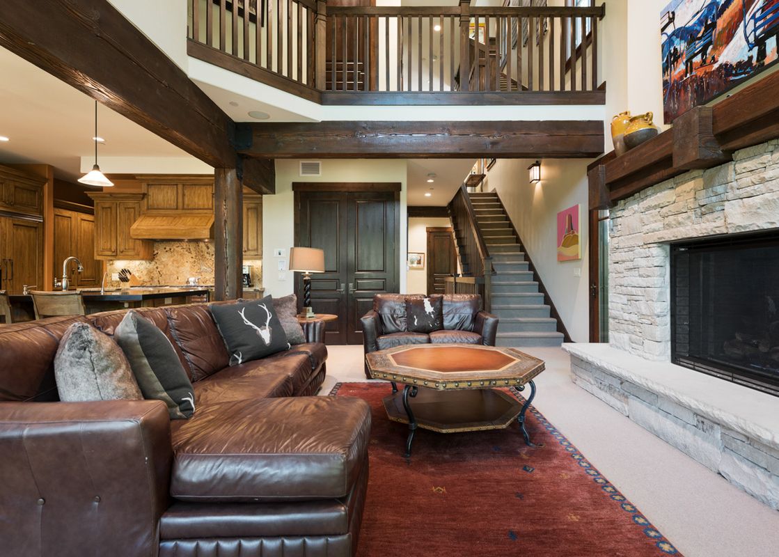 A spacious and inviting living area at Silver Star 15 with brown leather sofas, a unique octagonal coffee table, a red area rug, and a stone fireplace.