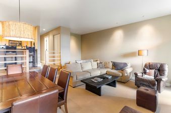 A living room with a beige sectional sofa, a coffee table with magazines and a remote, and a brown leather recliner.
