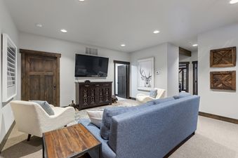 A cozy living room in Inspiration Ski Haus with a blue sofa, two cream armchairs, a large flat-screen TV, and framed artwork of a stag.