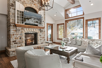 Grand Lodge Five Bedroom 402 living room with a fireplace, large windows with a view of the snowy mountains, and a cozy seating area.