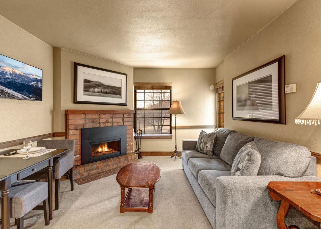 A cozy living room at Copperbottom 205 features a gray sofa, a fireplace, a dining table, and large window.