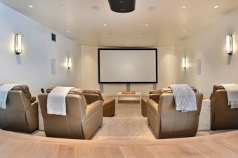 A home cinema with a large screen, several rows of comfortable brown leather recliners, and subtle lighting.