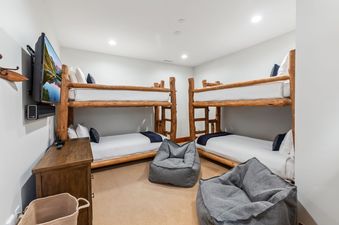 A bunk room at Blue Bird Vista at Hummingbird Lodge with two wooden bunk beds, white bedding, navy accents, bean bag chairs, and a wall-mounted TV.