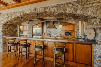 Luxurious rustic kitchen with a large stone arch, wooden bar, and high-end appliances at The Developers Residence at See Forever.