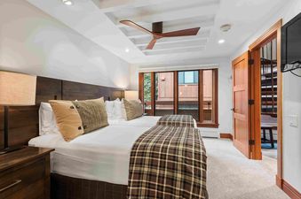 A guest bedroom with two twin beds, dark wooden headboards, plaid comforters, and a ceiling fan.