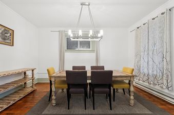 A brightly lit dining room with a large wooden table, eight chairs in dark brown and mustard yellow, and a modern rectangular chandelier.