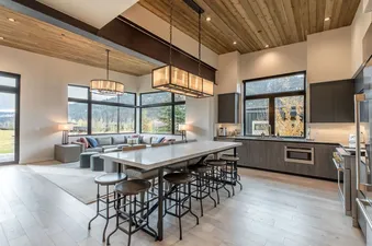 The Lodge Cabins' open-concept kitchen and living area feature dark cabinetry, a large island with bar stools, an L-shaped sofa, and expansive windows with mountain views.