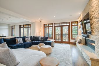 An elegant living area in Snow Cloud Lodge 509 with a navy sectional sofa, stone fireplace, and large windows offering an exterior view.