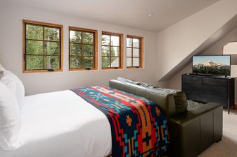 Moonlight Basin 7 Gambler features a bedroom with a king-size bed, a flat-screen TV, a couch, and views of the surrounding trees.