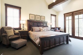 A spacious and inviting bedroom in Silver Star 04 features a grand wooden bed, elegant nightstands with classic lamps, and cozy armchairs, all bathed in natural light from multiple windows and balcony doors.