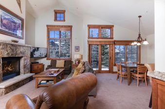 The living area of the Villa at Mountain Thunder features a stone fireplace, comfortable seating, and large windows with views of the snow-covered trees.