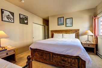 A hotel room bedroom with a large bed, bedside tables, and a window with a view outside.