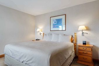 A queen-sized bed with white linens and pillows, flanked by wall-mounted lamps, is featured in a bedroom at The Charter L332, with a wooden nightstand to the right.