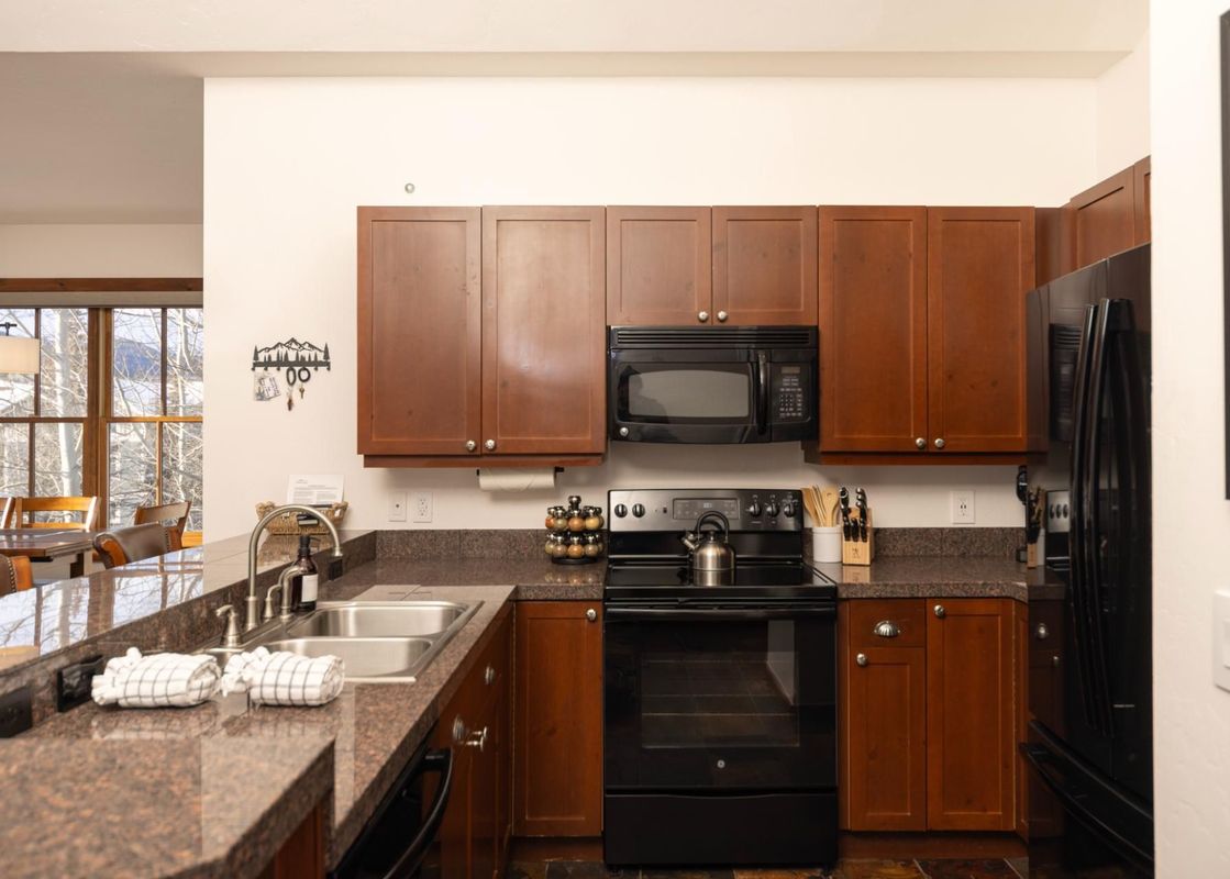 A modern kitchen with wood cabinets, black appliances, granite countertops, and a double sink.