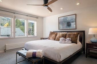 A modern and cozy bedroom in Hawks View Chalet featuring a king bed, bedside tables, and windows with scenic views of trees and hills.