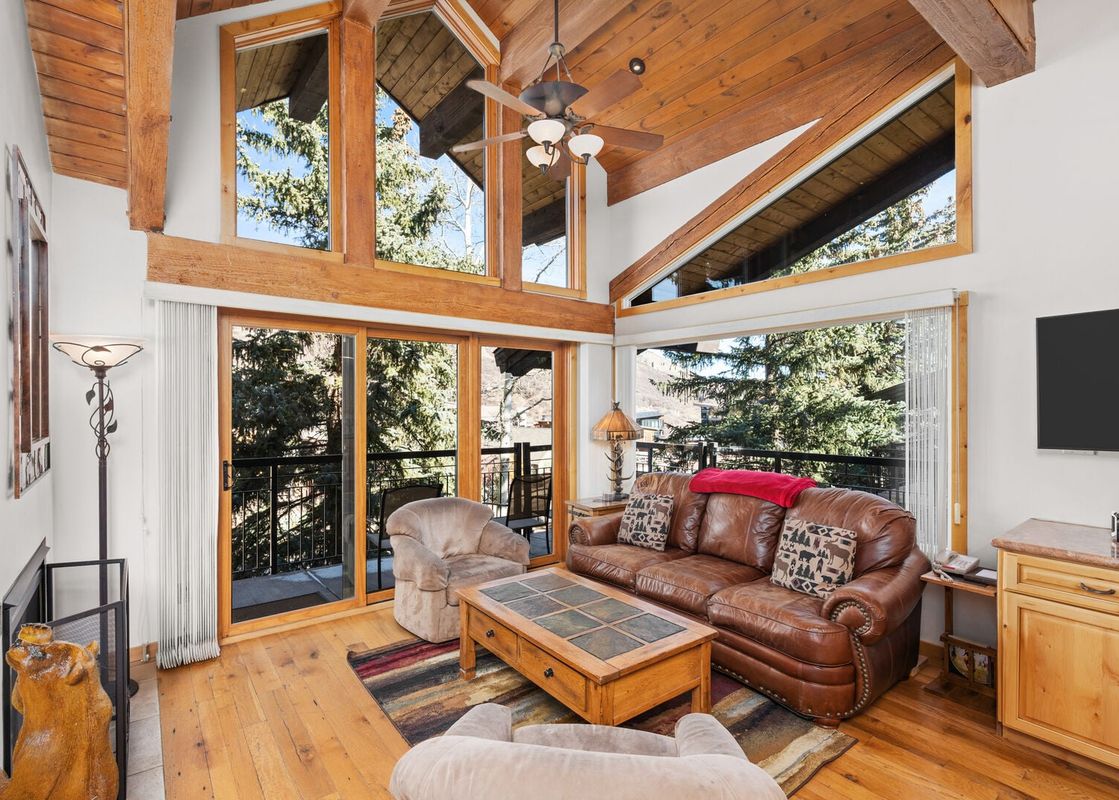 Living area of Crestwood 1212 with a brown leather sofa, large windows, and vaulted ceilings.