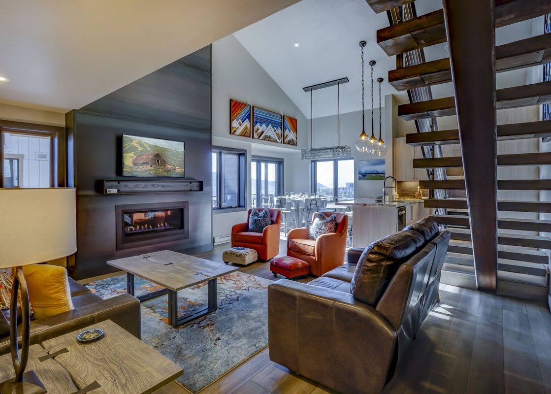 A living room with a fireplace, large windows, and a staircase.