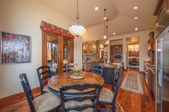 A dining area with a round wooden table and dark chairs, with a view of a living room and kitchen beyond.