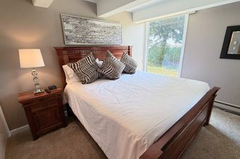 The bedroom at Vail International 002 features a comfortable bed with a wooden headboard, stylish throw pillows, and a bedside table with a lamp.