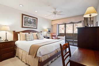 A cozy bedroom at St James Place 335 with a large bed, elegant wooden furniture, and a balcony offering a view of snow-covered trees.