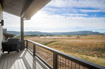 A private balcony at Keetly Vista with a BBQ grill and a panoramic view of hills and mountains under a partly cloudy sky.