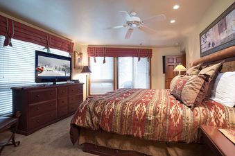 A luxurious bedroom at Chateau Chamonix CX115 with a large bed, patterned bedding, a flatscreen TV, and elegant window treatments.