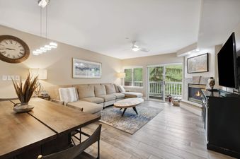 The inviting living area of St James Place 333 2BR, featuring a comfortable sectional sofa, a fireplace, and a large window overlooking lush greenery.