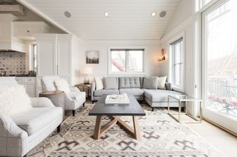 The bright and modern living room at Snowflake Villa features a grey sectional sofa, plaid armchairs, a dark coffee table, and an inviting ambiance with natural light and stylish decor.