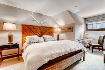 A bedroom with a king-sized bed, wooden headboard, and a window with a view of trees.