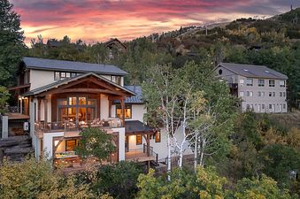 A multi-story house on a hillside at sunset, surrounded by trees.