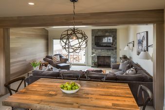 A modern living room with a large sectional sofa, a stone fireplace, and a wooden dining table.