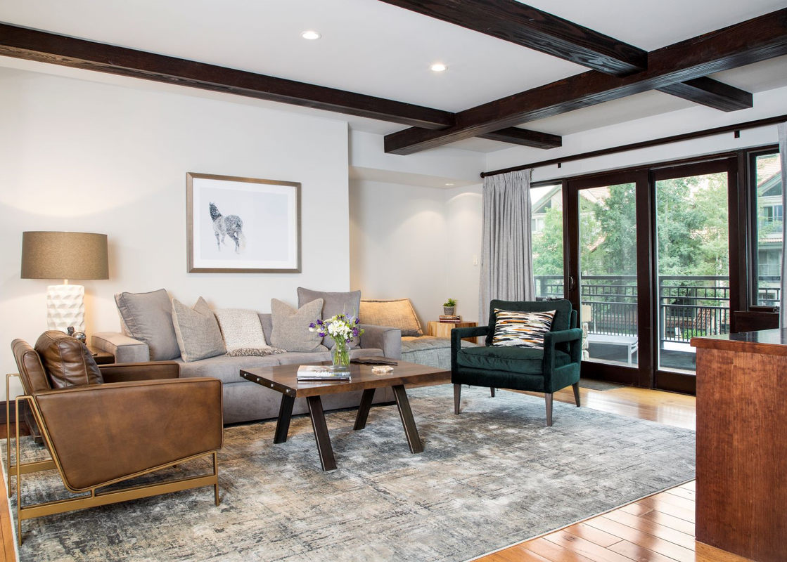 The living room of Lumiere Three Bedroom Unit 2 Bath features a grey couch, a coffee table, and a green armchair. The living room has a wood floor and a large window with a view of the outside.