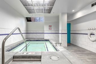 A bright and serene indoor hot tub area at Copperbottom Inn 102, featuring a clear water hot tub, white tiled walls with blue accents, and an overhead skylight.