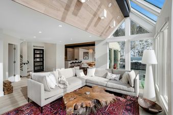 A spacious and modern living room at Luxe Lookout with a large L-shaped couch, a unique wooden coffee table, and expansive windows offering views of snow-covered trees.
