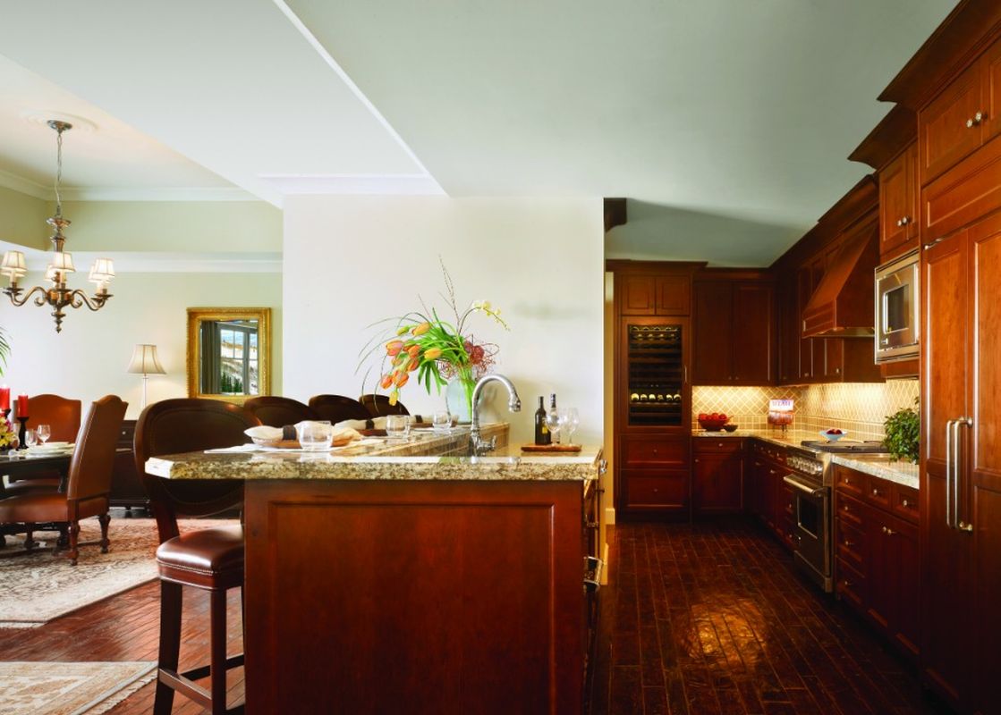 A large kitchen and dining area in the Montage Four Bedroom Residence Summit View feature dark wood cabinetry, stainless steel appliances, a long kitchen island with bar seating, and a formal dining table with upholstered chairs.