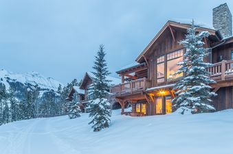 A luxurious ski-in, ski-out mountain suite, Big View Luxury Suite, in a snowy landscape with stunning mountain views, featuring warm interior lights and a hot tub on the deck.
