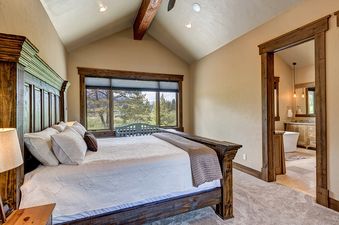 A bedroom with a king size bed, a view of the mountains, and a door leading to a bathroom.